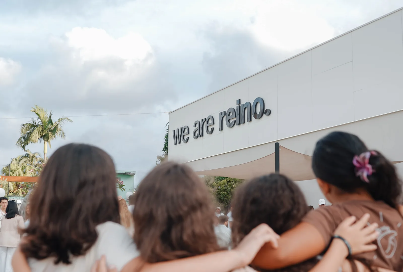 Grupo abraçado, de costas, olhando para o letreiro we are reino