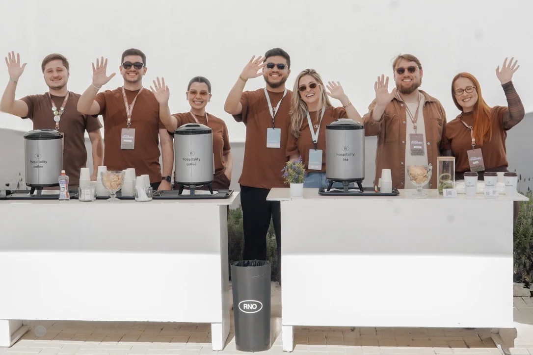 Equipe de voluntários do hospitality acenando atrás das mesas de café no pátio