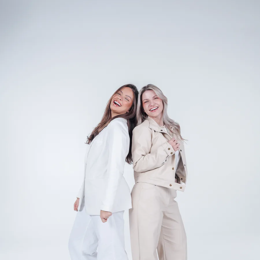 Duas amigas abraçadas, de branco, no estúdio