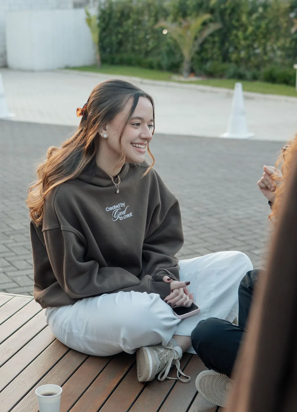 Mulher de moletom marrom sentada no deck, conversando, com o café ao lado