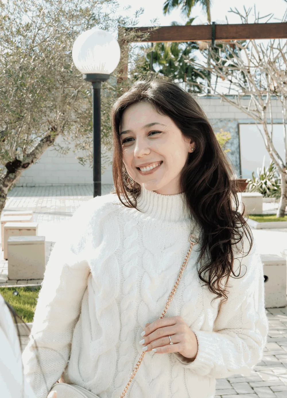 Mulher de tricô branco sorri no pátio, sob a pérgola