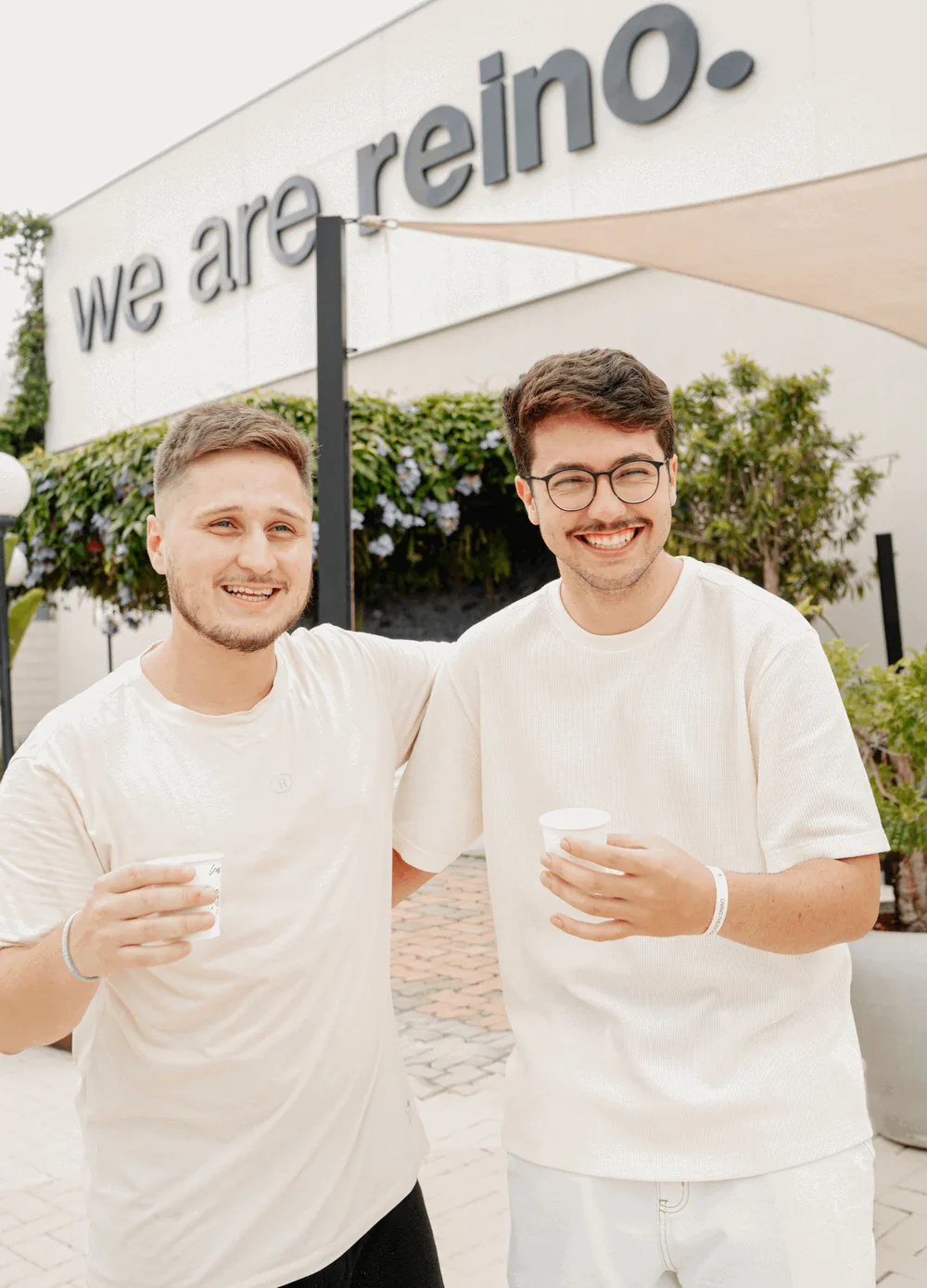 Dois amigos com café, de frente para o letreiro